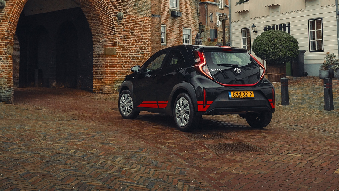 Toyota-Aygo-X-exterieur-driekwart-achter-zwart-rood-voor-oude-stadspoort-
